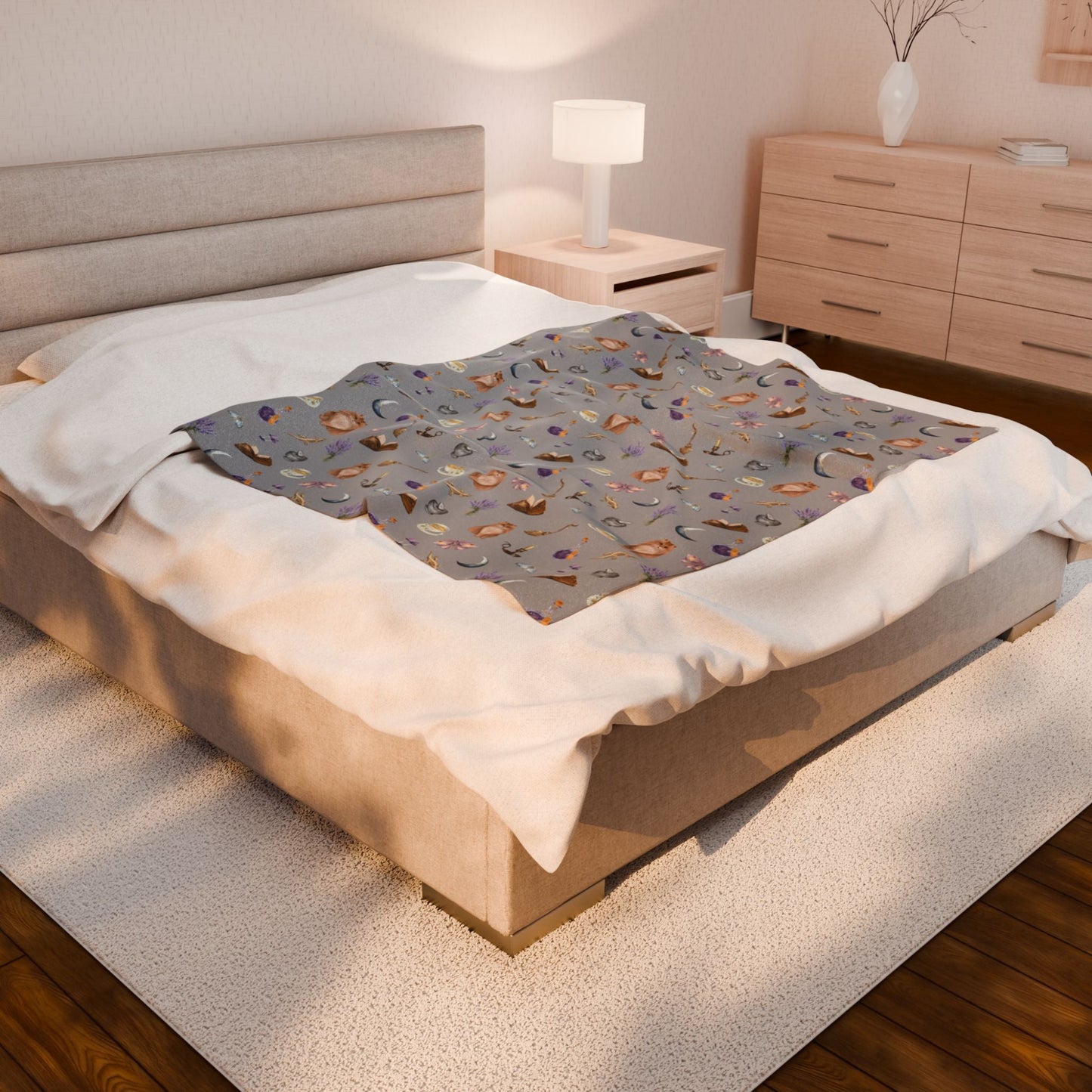 cozy bed decorated with printed throw blanket featuring witchy aesthetic cats, brooms, cauldrons, herbs, potions, moths, and mushrooms