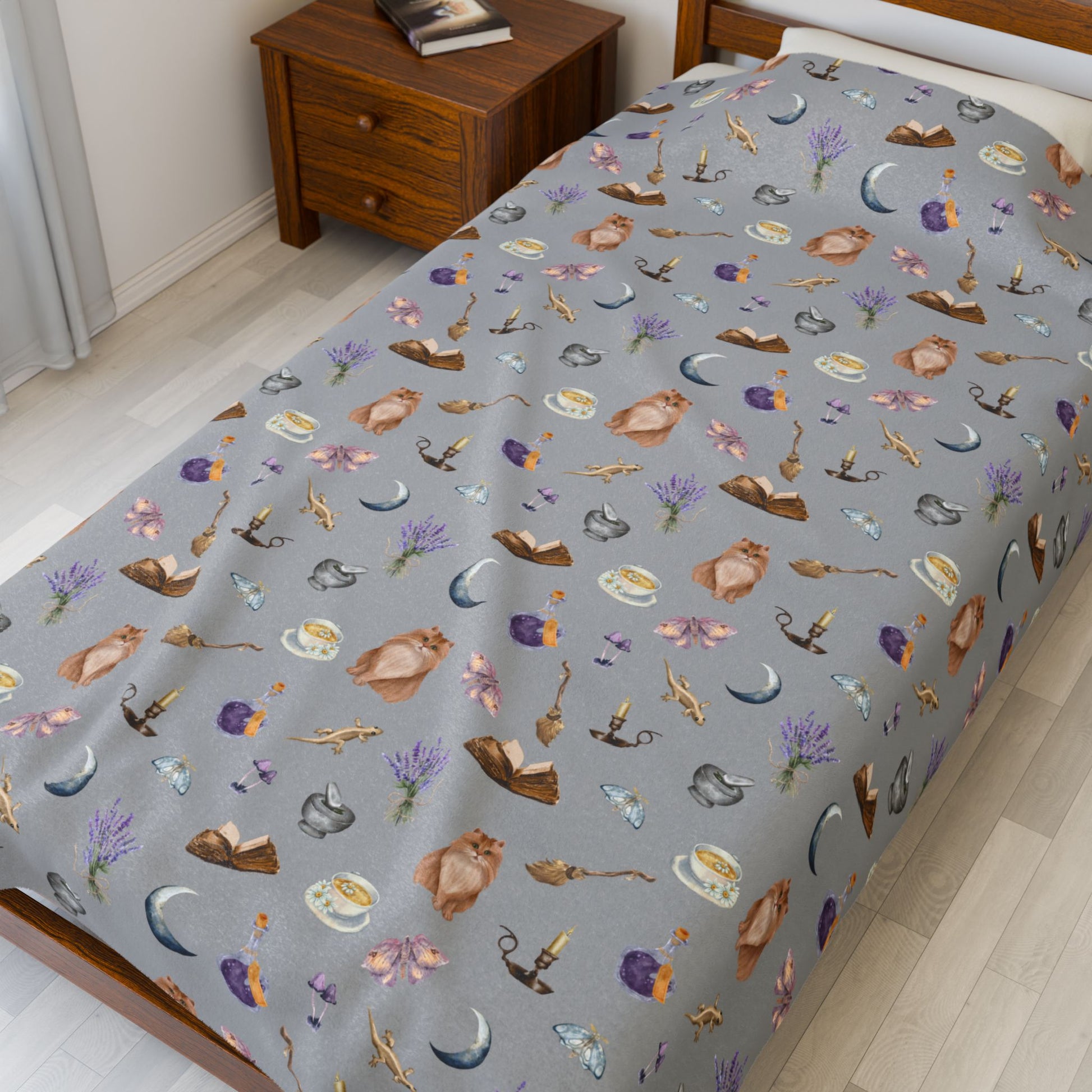 Patterned Halloween throw blanket featuring cats, books, tea cups, broomsticks, candles, lavender, and moths on a twin bed
