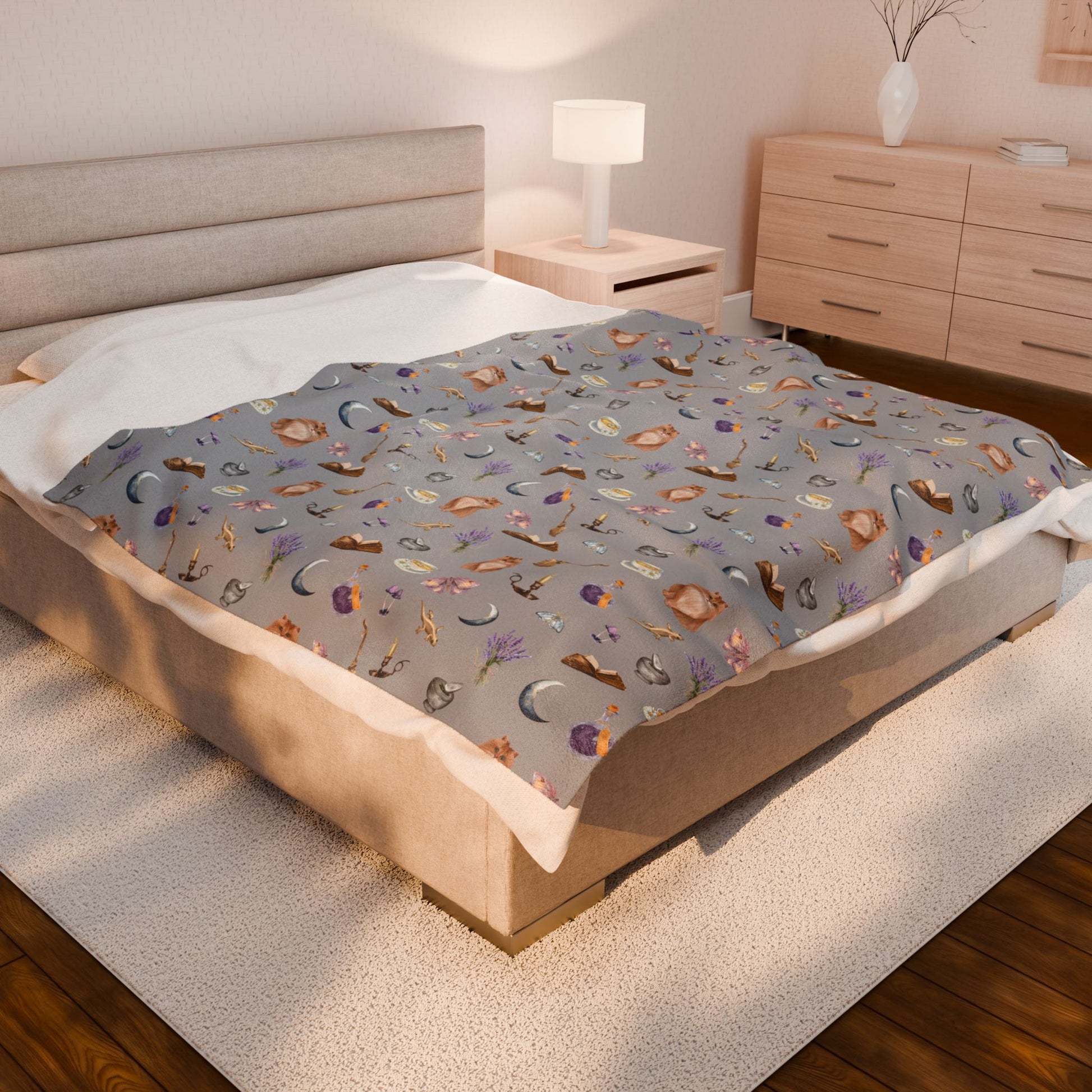 Patterned Halloween throw blanket featuring cats, books, tea cups, broomsticks, candles, lavender, and moths on a queen bed